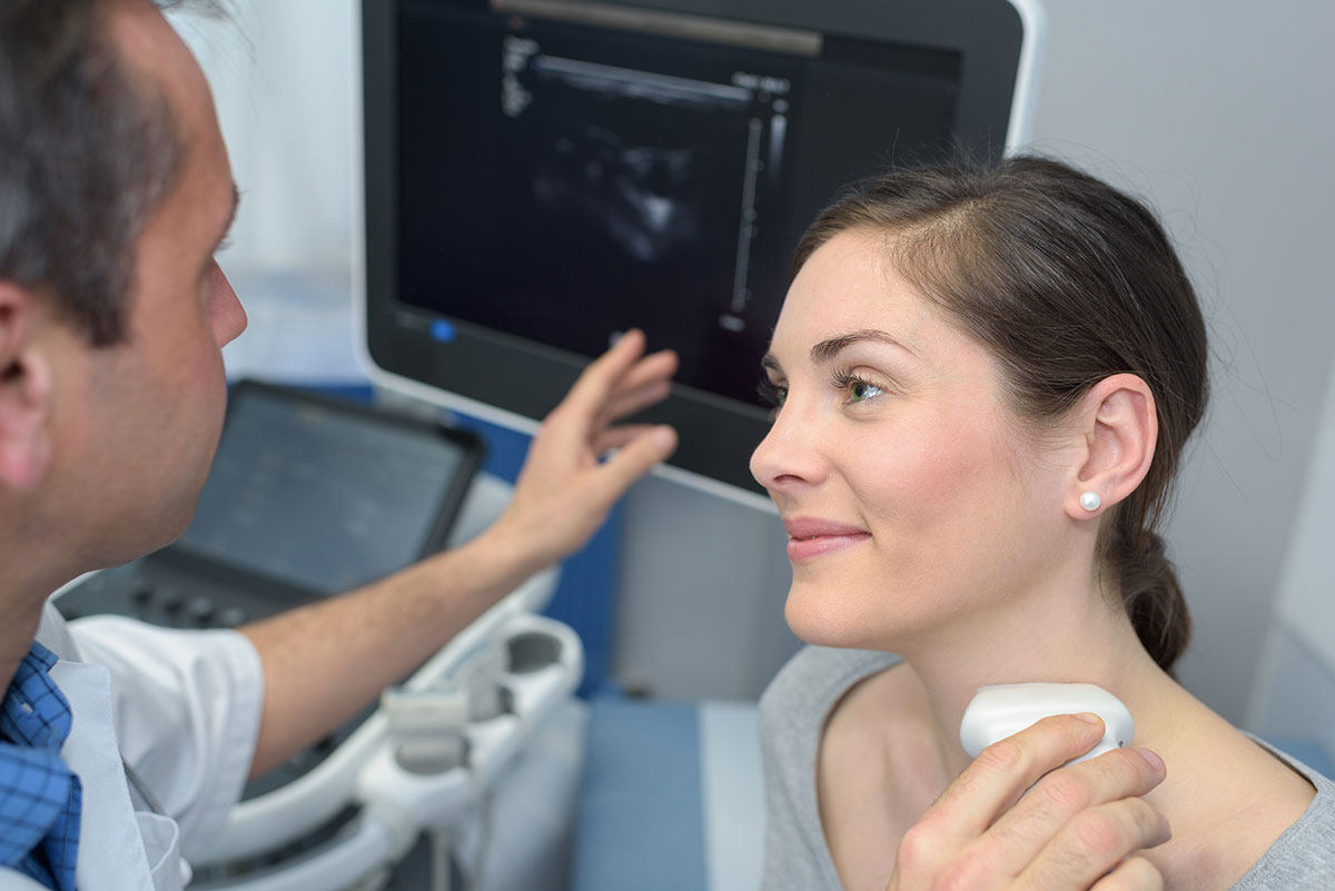 Ein Arzt untersucht mit einem Ultraschallgerät die Schilddrüse einer Frau.